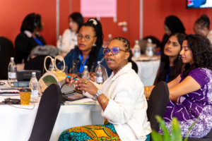 Convening participants around a table, a woman at the centre of the frame is talking. Behind her is Aishwarya Rajeev, Finance Sector Lead at Global 50/50, and Global 50/50 Justice Sector lead, Govindi Deerasinghe